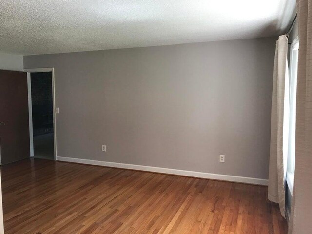 spare room featuring wood finished floors, baseboards, and a textured ceiling