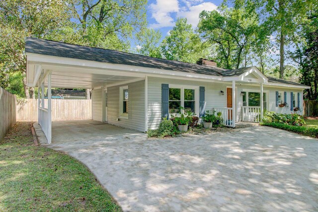 ranch-style home featuring a carport, driveway, a chimney, covered porch, and fence