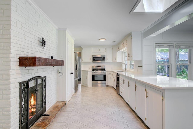 kitchen featuring stainless steel appliances, light countertops, a peninsula, ornamental molding, and a brick fireplace
