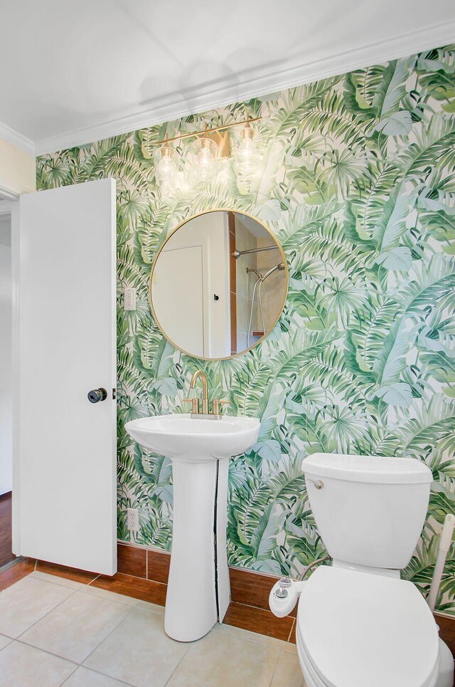 half bath with tile patterned floors, toilet, baseboards, wallpapered walls, and ornamental molding