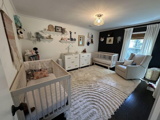 bedroom with a nursery area, wood finished floors, visible vents, and crown molding