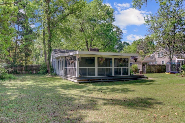 rear view of house featuring a lawn, a fenced backyard, a chimney, and a sunroom