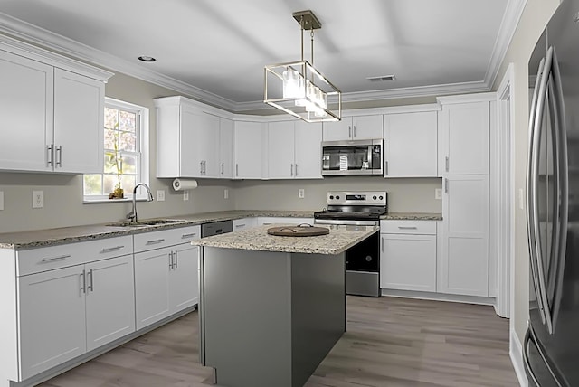 kitchen with white cabinets, appliances with stainless steel finishes, ornamental molding, a center island, and a sink