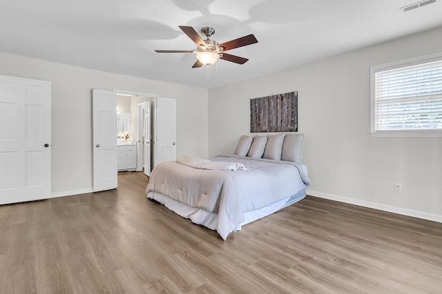 bedroom featuring visible vents, wood finished floors, baseboards, a ceiling fan, and ensuite bath