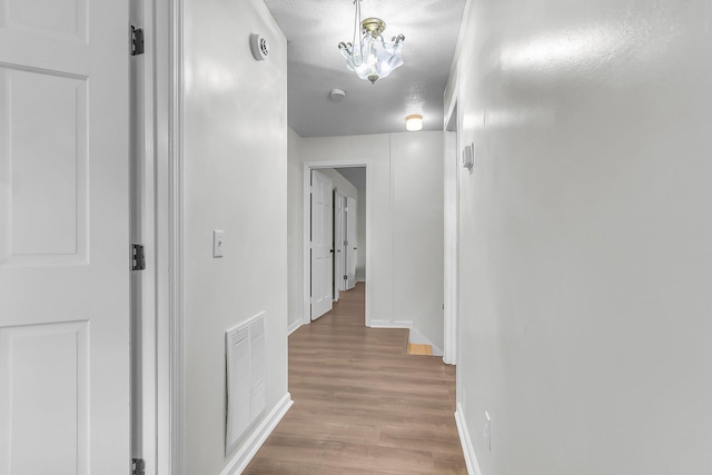 hall featuring a notable chandelier, visible vents, baseboards, and light wood finished floors