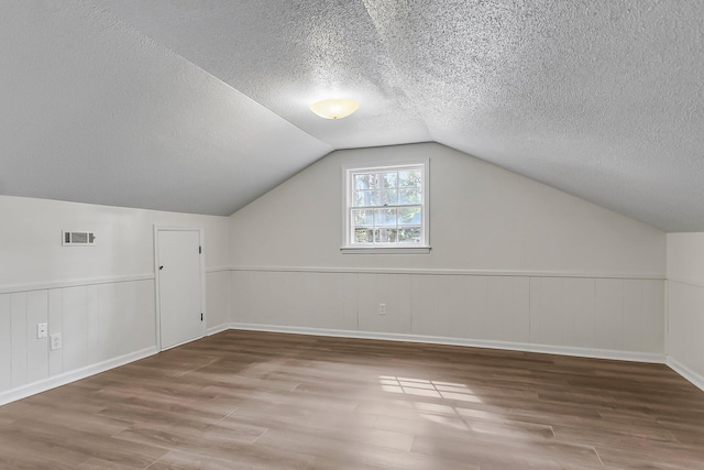 bonus room featuring a textured ceiling, visible vents, wainscoting, vaulted ceiling, and wood finished floors