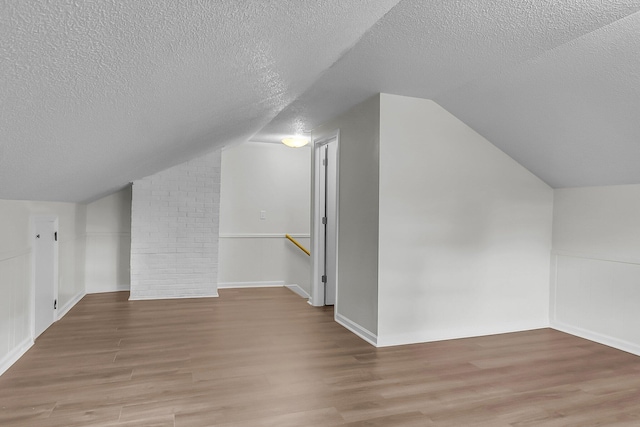 additional living space with baseboards, a textured ceiling, light wood finished floors, and lofted ceiling