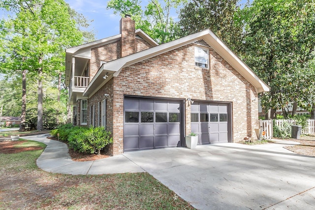 view of side of property with a chimney, an attached garage, concrete driveway, and brick siding