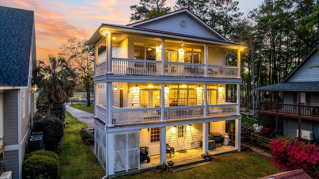 back house at dusk featuring a patio, a balcony, and french doors