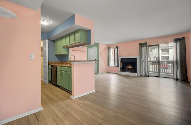 kitchen featuring baseboards, light wood finished floors, dishwasher, green cabinets, and open floor plan