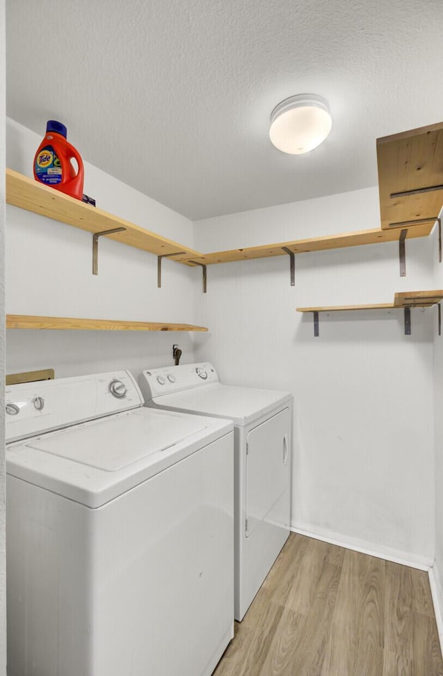 laundry room with laundry area, separate washer and dryer, light wood-style floors, and a textured ceiling