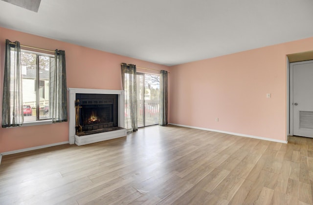 unfurnished living room featuring a wealth of natural light, light wood-style flooring, a warm lit fireplace, and baseboards