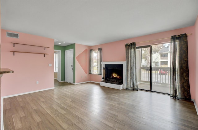 unfurnished living room with visible vents, baseboards, a brick fireplace, and light wood-style flooring