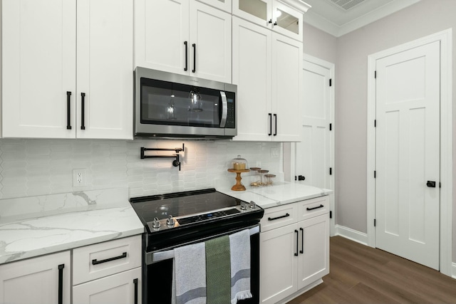 kitchen with electric range, glass insert cabinets, stainless steel microwave, light stone counters, and white cabinetry