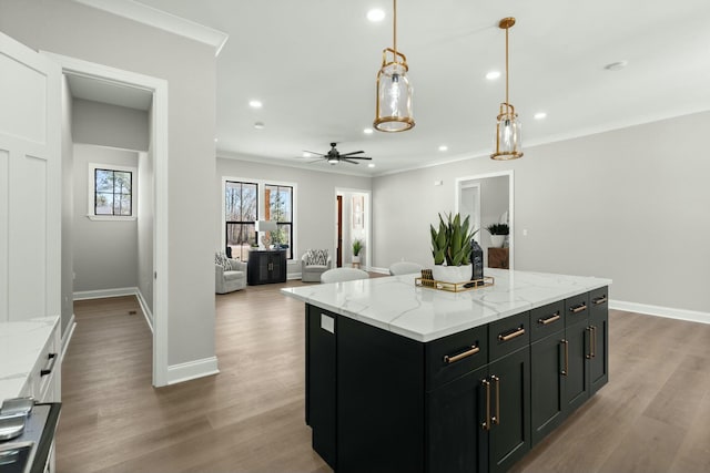 kitchen featuring a kitchen island, open floor plan, dark cabinetry, light stone countertops, and crown molding