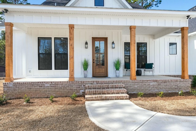 doorway to property with a porch, board and batten siding, and roof with shingles