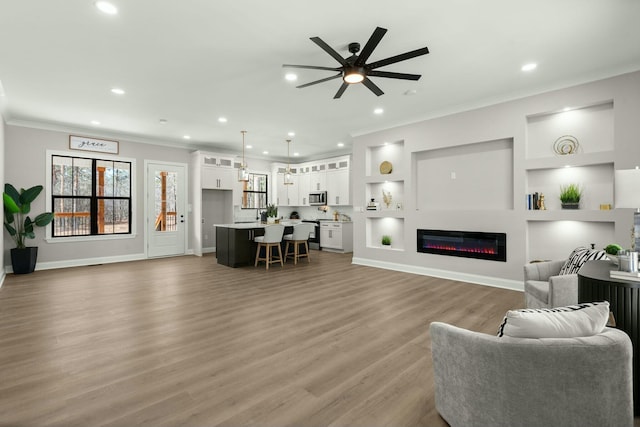 living room featuring built in features, recessed lighting, ornamental molding, a glass covered fireplace, and wood finished floors