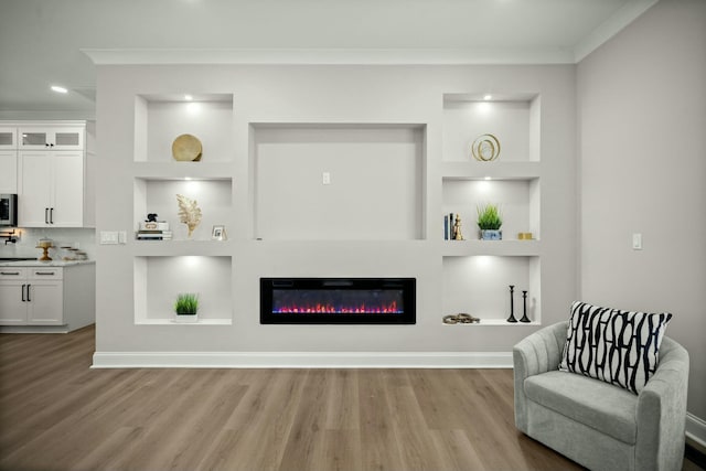 living area featuring baseboards, built in features, light wood finished floors, a glass covered fireplace, and crown molding