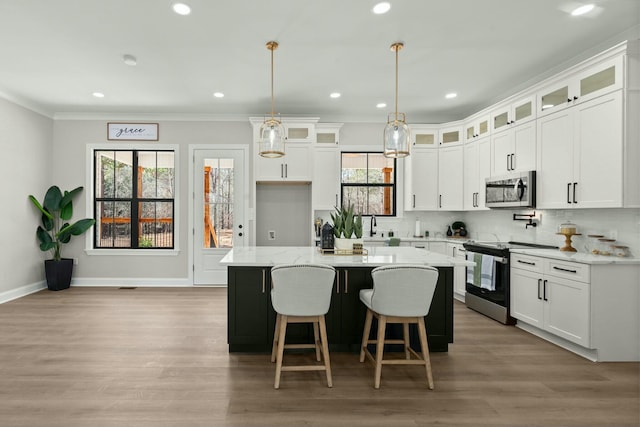 kitchen with appliances with stainless steel finishes, glass insert cabinets, a kitchen island, and white cabinetry