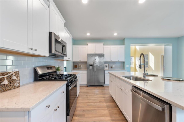 kitchen featuring white cabinetry, sink, stainless steel appliances, light stone counters, and light wood-type flooring