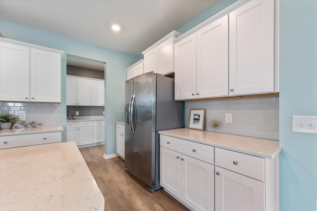 kitchen with decorative backsplash, stainless steel fridge, light hardwood / wood-style floors, light stone counters, and white cabinetry