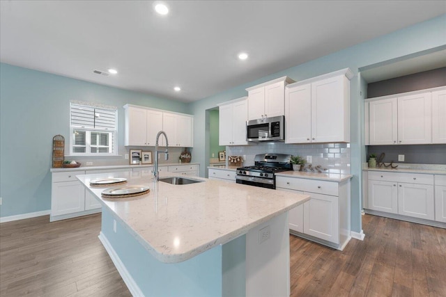 kitchen featuring dark hardwood / wood-style flooring, stainless steel appliances, sink, white cabinets, and an island with sink