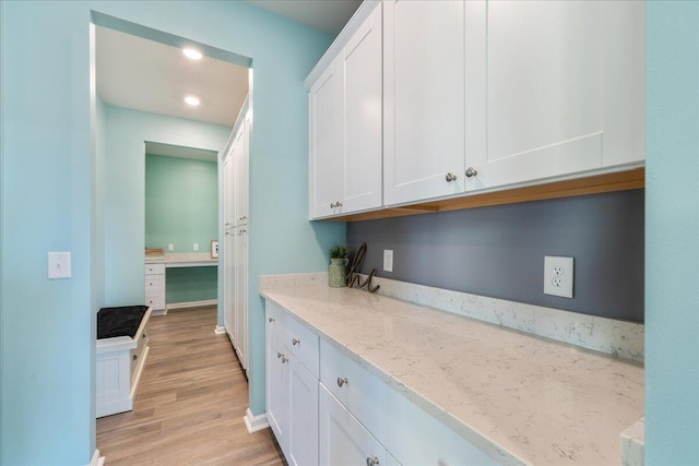 kitchen with white cabinets, light wood-type flooring, and light stone counters