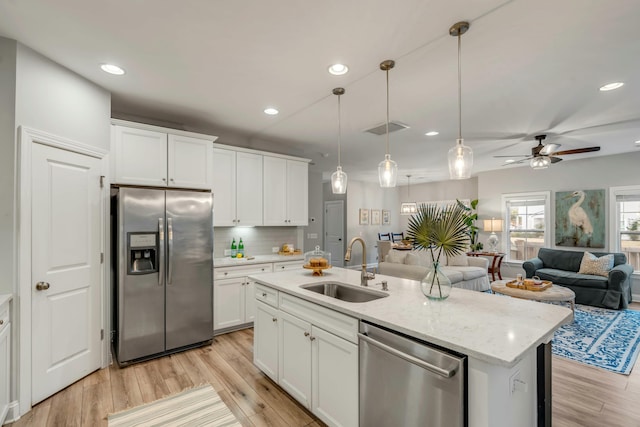 kitchen with white cabinets, stainless steel appliances, an island with sink, sink, and hanging light fixtures