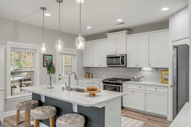 kitchen featuring appliances with stainless steel finishes, tasteful backsplash, sink, a kitchen island with sink, and light stone counters