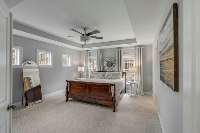 bedroom featuring ceiling fan, multiple windows, a tray ceiling, and light carpet