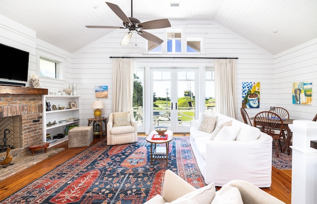 living room with wood-type flooring, a wealth of natural light, wooden walls, and a brick fireplace