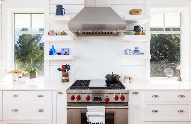 kitchen featuring high end range, ventilation hood, white cabinets, and a wealth of natural light