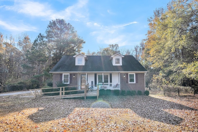 new england style home with covered porch, brick siding, and fence