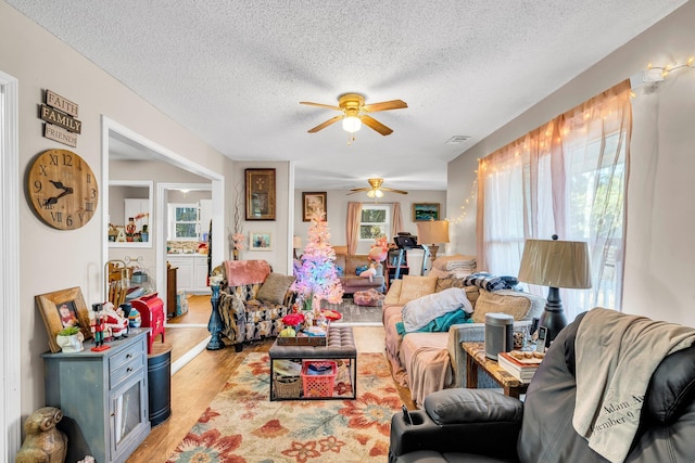 living room featuring a textured ceiling, a ceiling fan, visible vents, and light wood-style floors