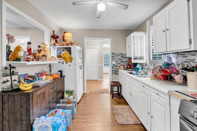 kitchen with light countertops, freestanding refrigerator, white cabinets, a sink, and light wood-type flooring