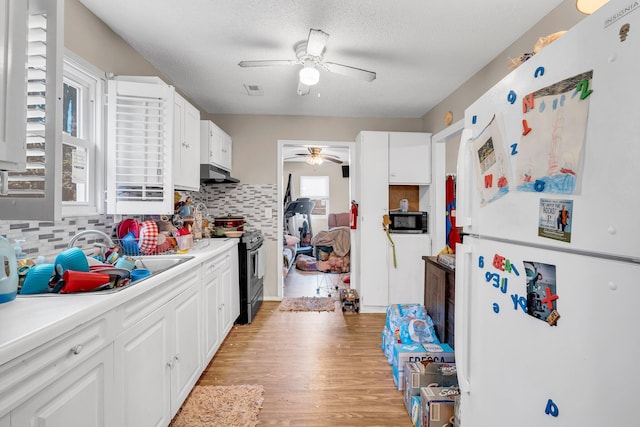 kitchen featuring freestanding refrigerator, stainless steel range oven, light wood-type flooring, black microwave, and under cabinet range hood