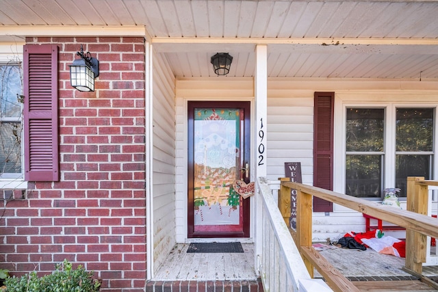 doorway to property with covered porch and brick siding