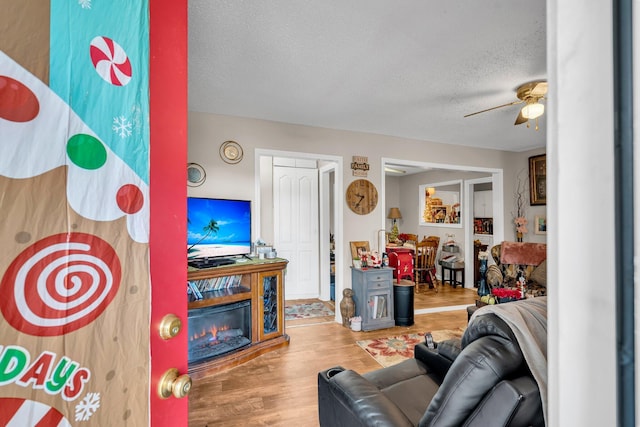 living room with a glass covered fireplace, ceiling fan, a textured ceiling, and wood finished floors