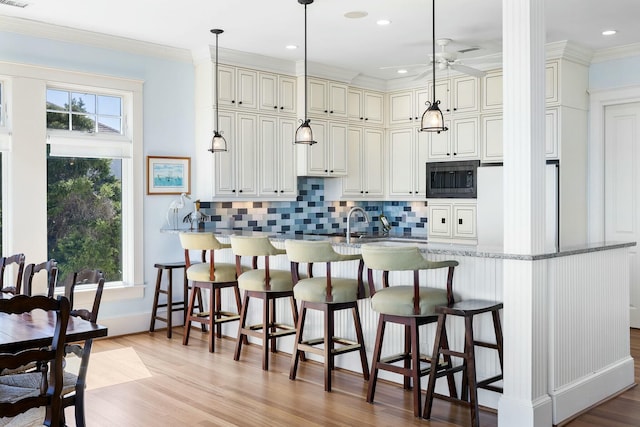 kitchen with a wealth of natural light, ornamental molding, black microwave, and freestanding refrigerator