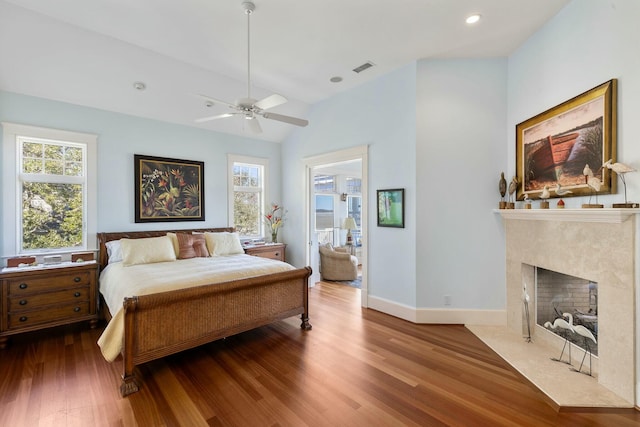 bedroom featuring multiple windows, lofted ceiling, wood finished floors, and a high end fireplace