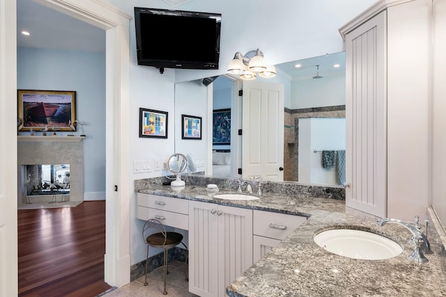 full bath featuring a sink, a multi sided fireplace, wood finished floors, and double vanity