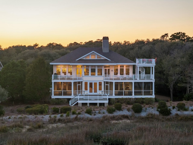 back of house at dusk with a balcony and a chimney