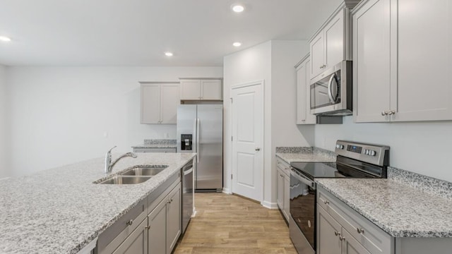 kitchen featuring a center island with sink, sink, light stone countertops, appliances with stainless steel finishes, and light hardwood / wood-style floors