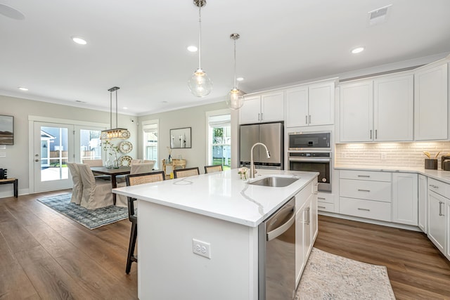 kitchen featuring dark hardwood / wood-style flooring, stainless steel appliances, an island with sink, ornamental molding, and sink