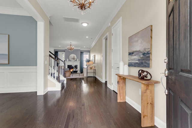 foyer with a notable chandelier, ornamental molding, and dark wood-type flooring