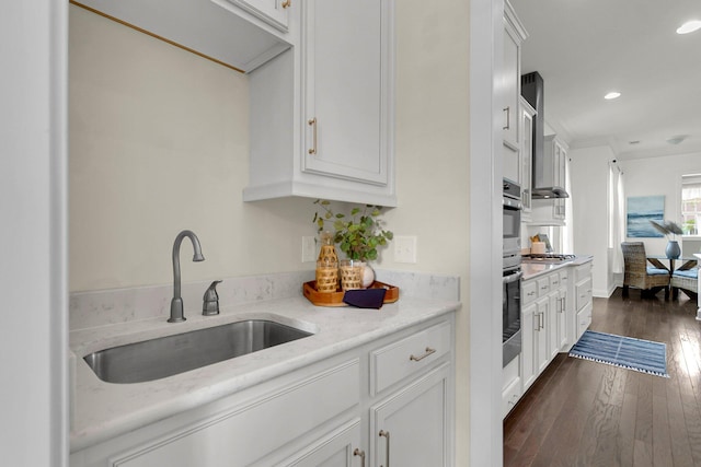 kitchen with sink, wall chimney exhaust hood, stainless steel appliances, dark hardwood / wood-style floors, and white cabinets