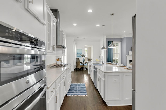 kitchen featuring stainless steel appliances, wall chimney range hood, sink, pendant lighting, and white cabinets