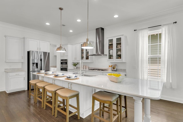 kitchen with sink, wall chimney exhaust hood, hanging light fixtures, an island with sink, and appliances with stainless steel finishes