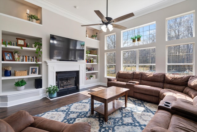 living area with built in features, ornamental molding, a fireplace, wood finished floors, and a ceiling fan