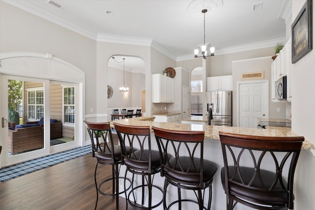 kitchen featuring visible vents, an inviting chandelier, a peninsula, arched walkways, and appliances with stainless steel finishes